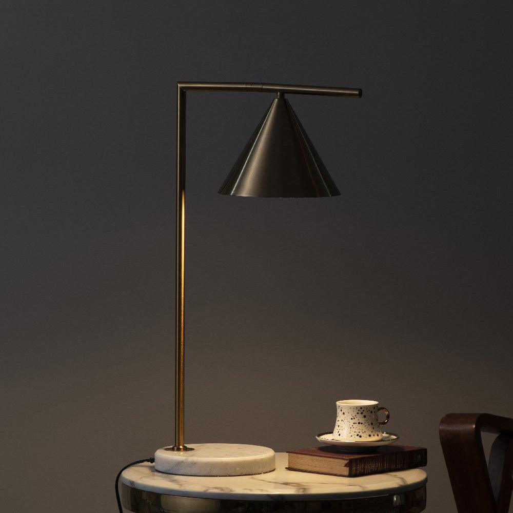In a dimly lit scene, the Clérachic lamp sits beside a stacked book and a teacup and saucer on a round marble side table.