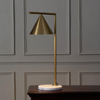 Clérachic's cone-shade table lamp stands on a dark wood console against a grey wainscoted wall, its stem catching soft side light.