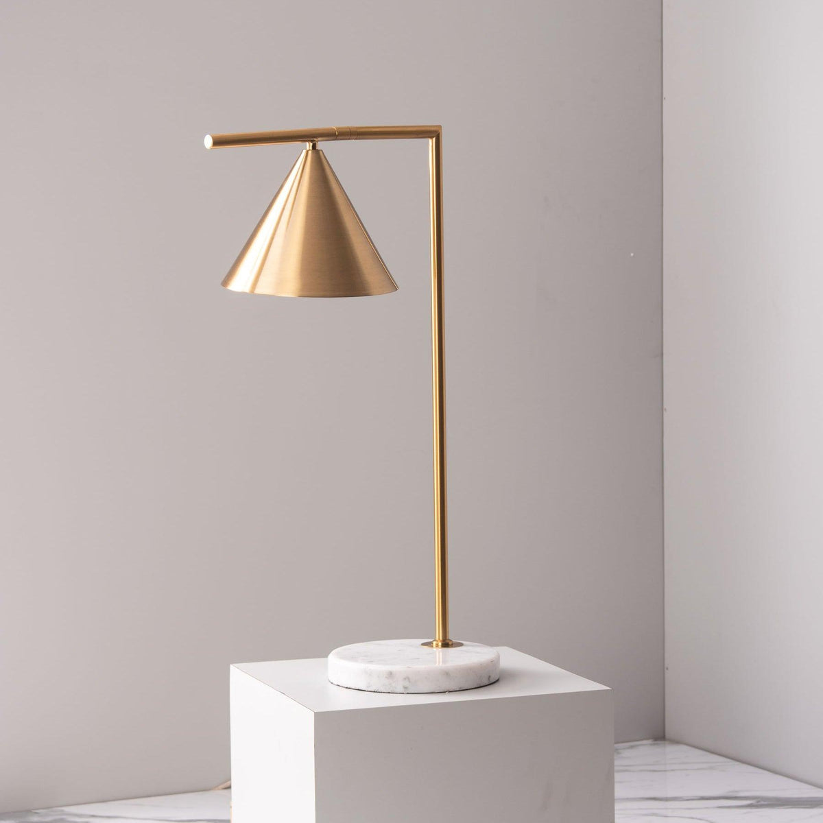 Raised on a white plinth against a bare wall, this minimal shot isolates the Clérachic lamp's brass frame and cone shade.