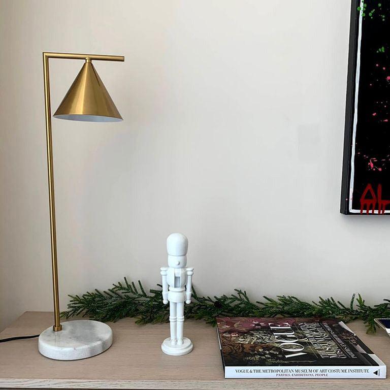 Styled for the season, the Clérachic lamp sits on a light wood table beside a small white nutcracker figure and magazines.
