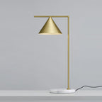Photographed from a low angle, the Clérachic lamp's tall brass stem rises against a blue-grey backdrop, its cord trailing below.