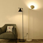 Black floor lamp with opal cone beside a minimalist armchair