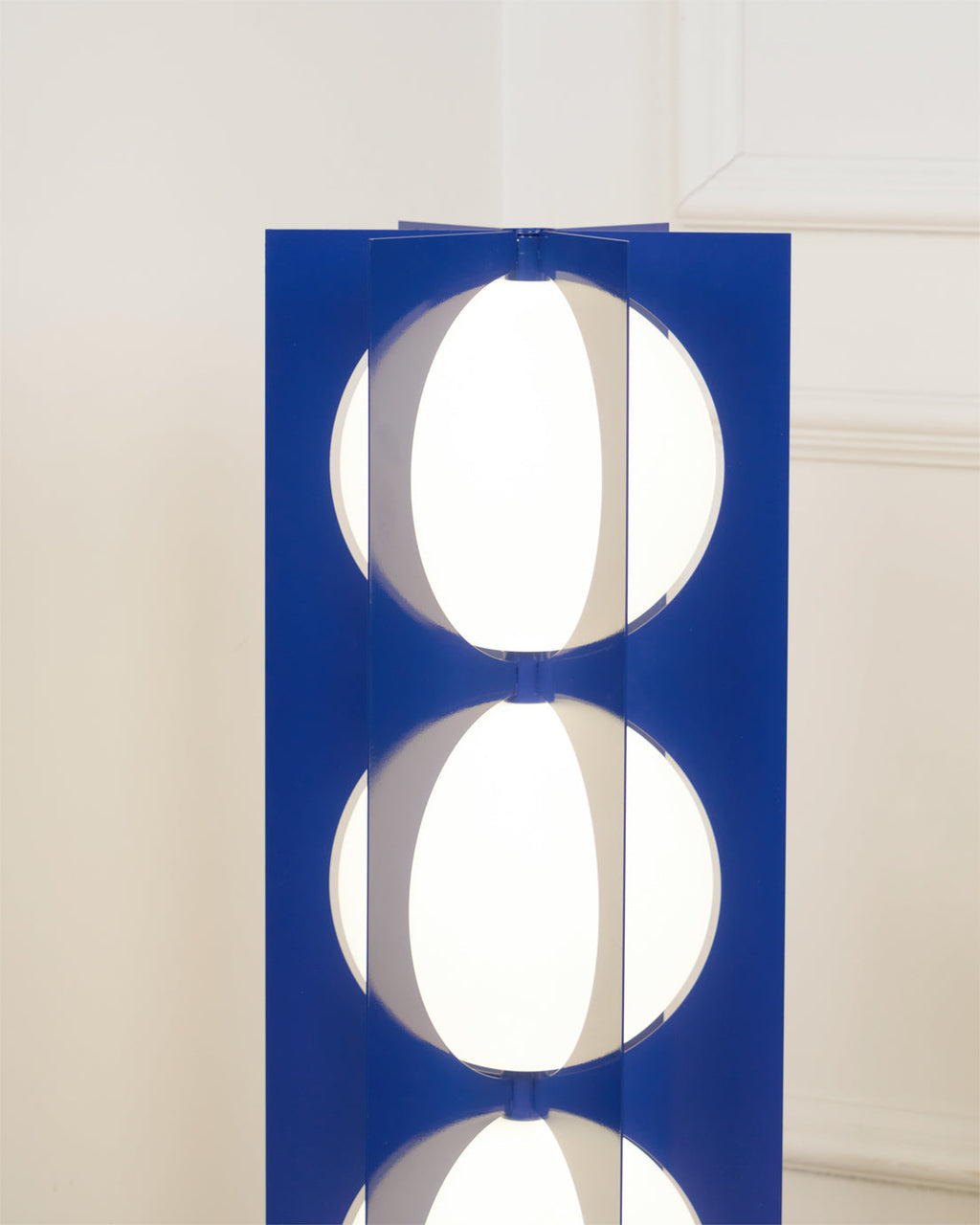 Close-up of two stacked glass globes glowing between the Clérachic floor lamp's navy metal fins.