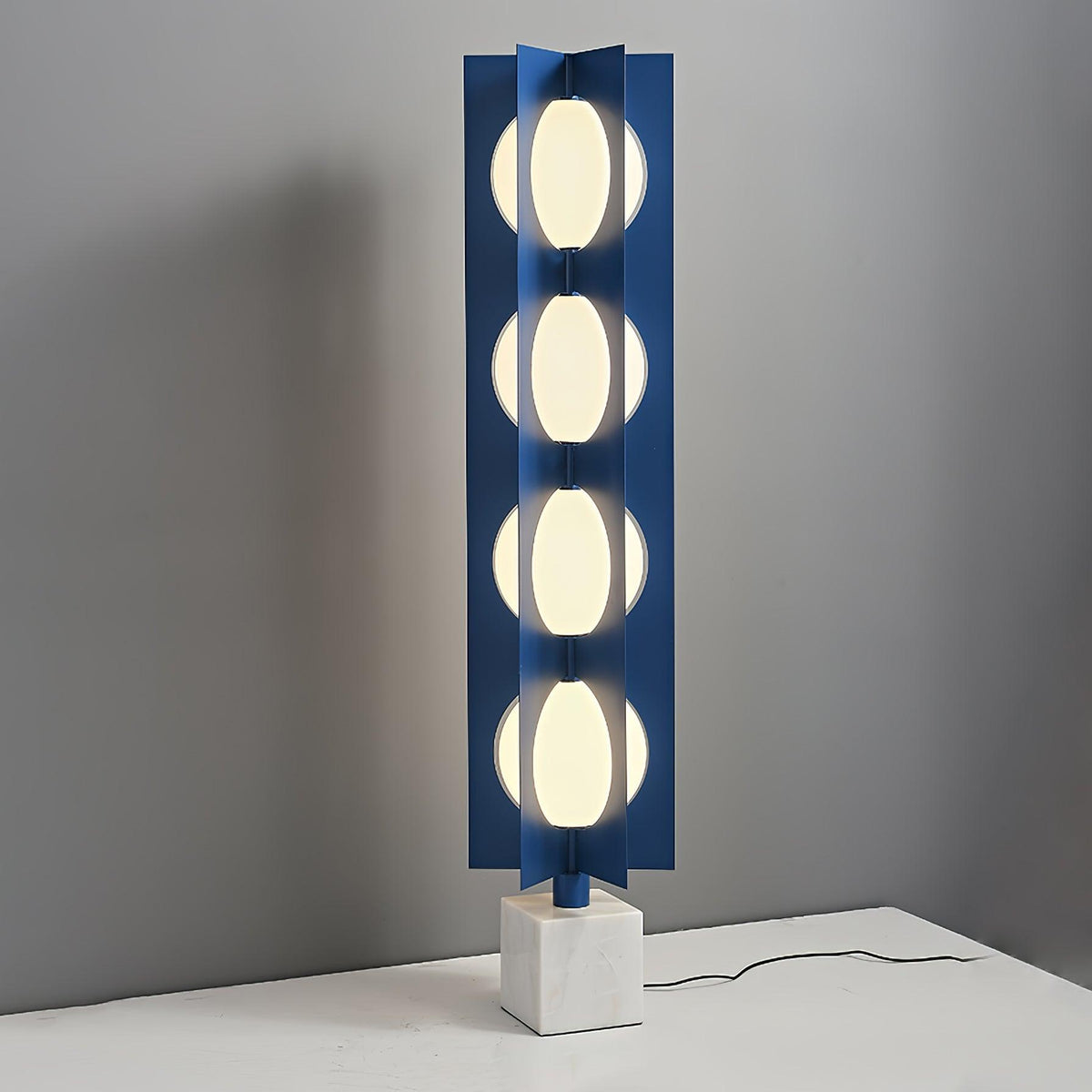 Four-globe Clérachic floor lamp on a pale square base, standing on a white surface against a plain grey wall.