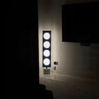 Four-globe Clérachic floor lamp glowing in a darkened room beside a blank wall-mounted television screen.