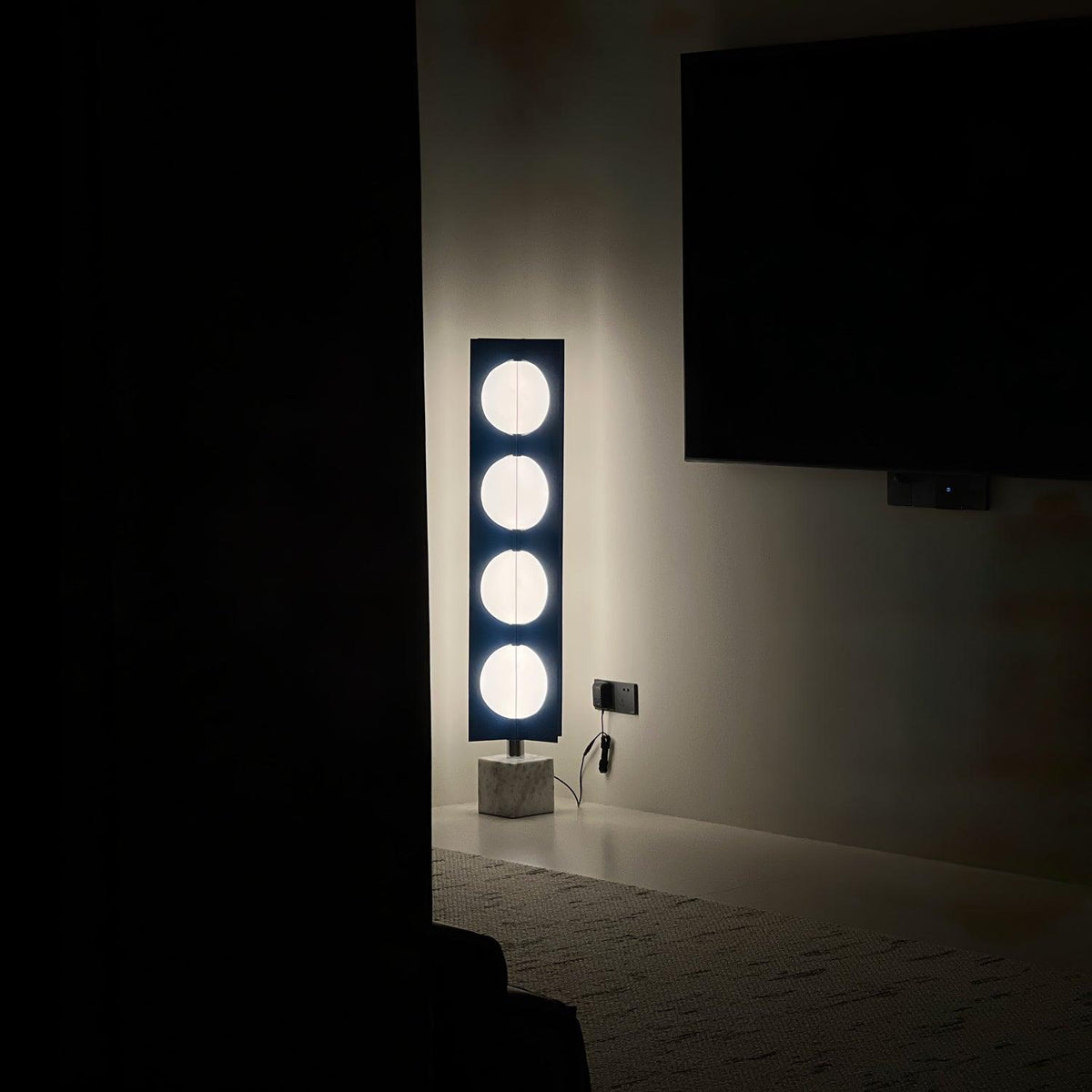 Four-globe Clérachic floor lamp glowing in a darkened room beside a blank wall-mounted television screen.