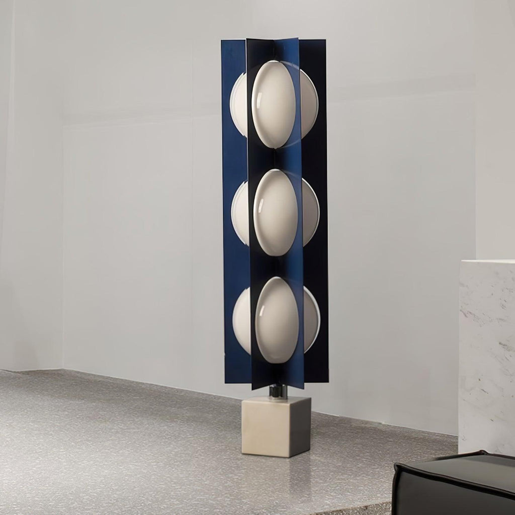 Three-globe Clérachic lamp on a warm stone base, standing on a coarse sandy-textured surface against a plain wall.