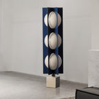 Three-globe Clérachic lamp on a warm stone base, standing on a coarse sandy-textured surface against a plain wall.