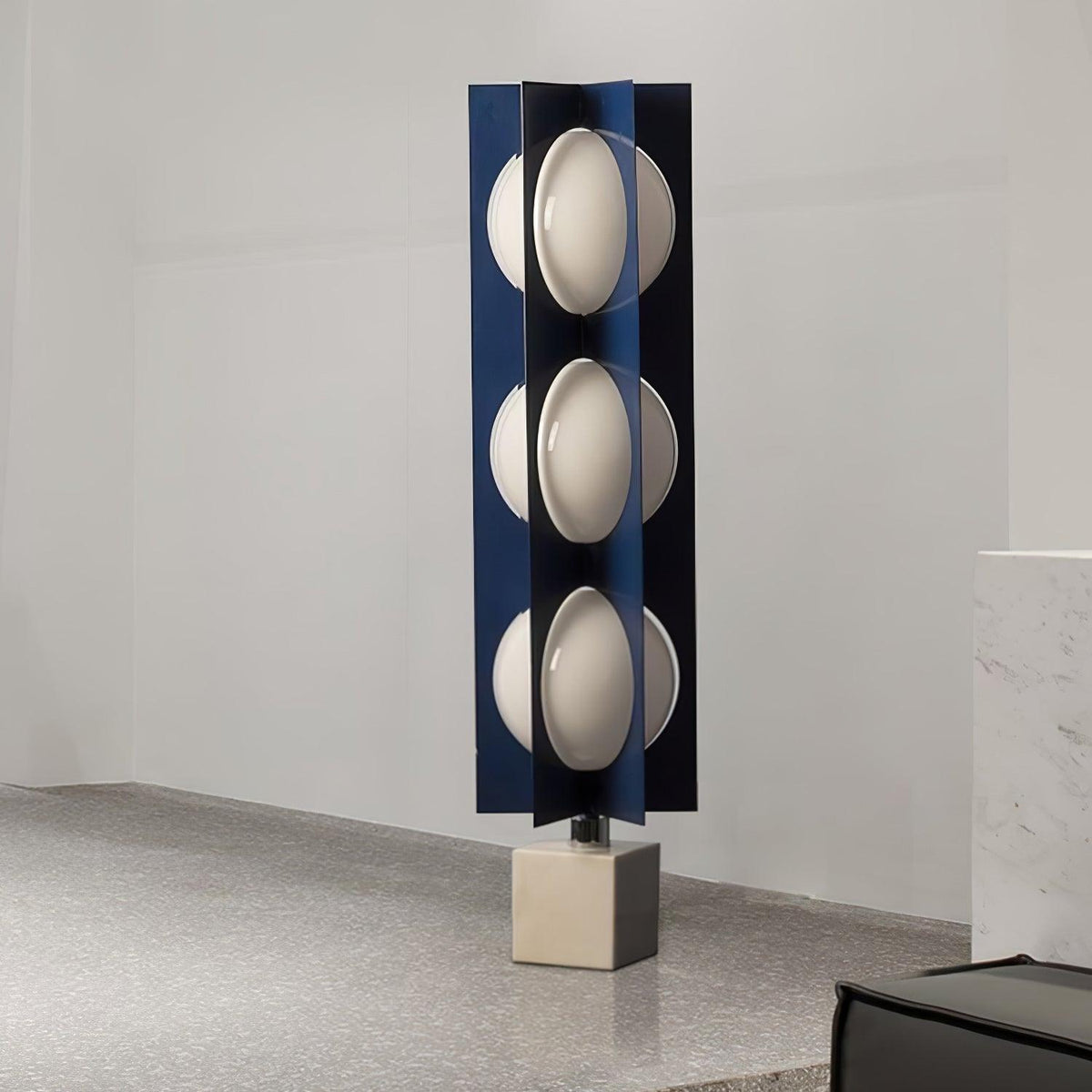 Three-globe Clérachic lamp on a warm stone base, standing on a coarse sandy-textured surface against a plain wall.