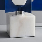 Close-up of the Clérachic lamp's chrome collar and navy fins meeting a veined white marble cube base.