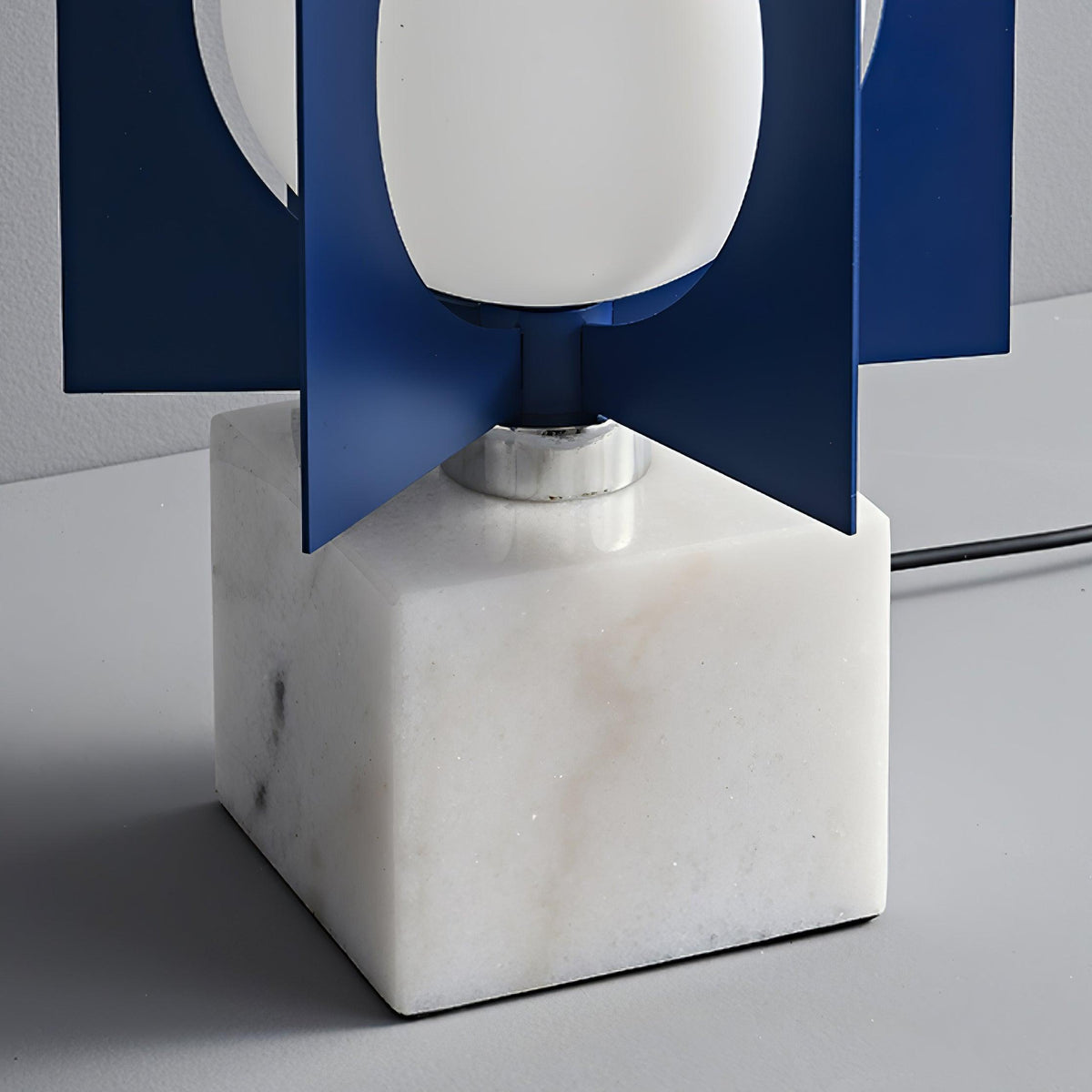 Close-up of the Clérachic lamp's oval shade and chrome collar seated on a veined white marble cube base.