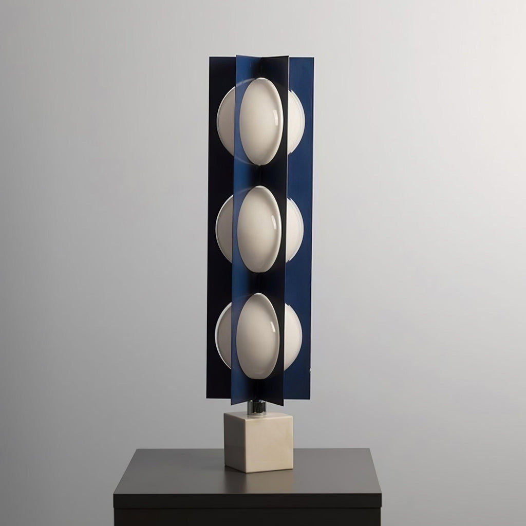 Three-globe Clérachic lamp on a warm stone base, standing on a dark wood nightstand against a plain grey wall.