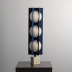 Three-globe Clérachic lamp on a warm stone base, standing on a dark wood nightstand against a plain grey wall.