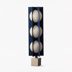 Three-globe Clérachic lamp in dark navy on a warm stone base, shown unlit in a tight studio crop.