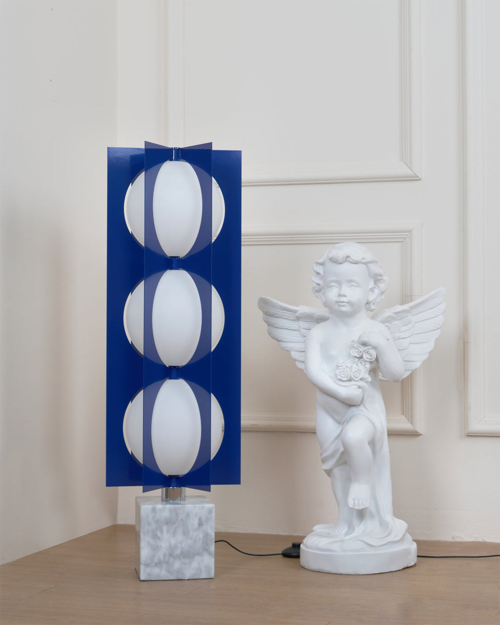 Three-globe Clérachic floor lamp on a white marble base, shown in full beside a cherub statue near a panelled door.