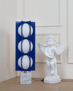 Three-globe Clérachic floor lamp on a white marble base, shown in full beside a cherub statue near a panelled door.