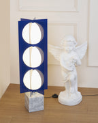 Three-globe Clérachic lamp lit beside a cherub statue, framed within a panelled doorway in a warm-toned room.