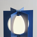 Close-up of the Clérachic floor lamp's egg-shaped glass shade glowing between two navy metal fins at the join.