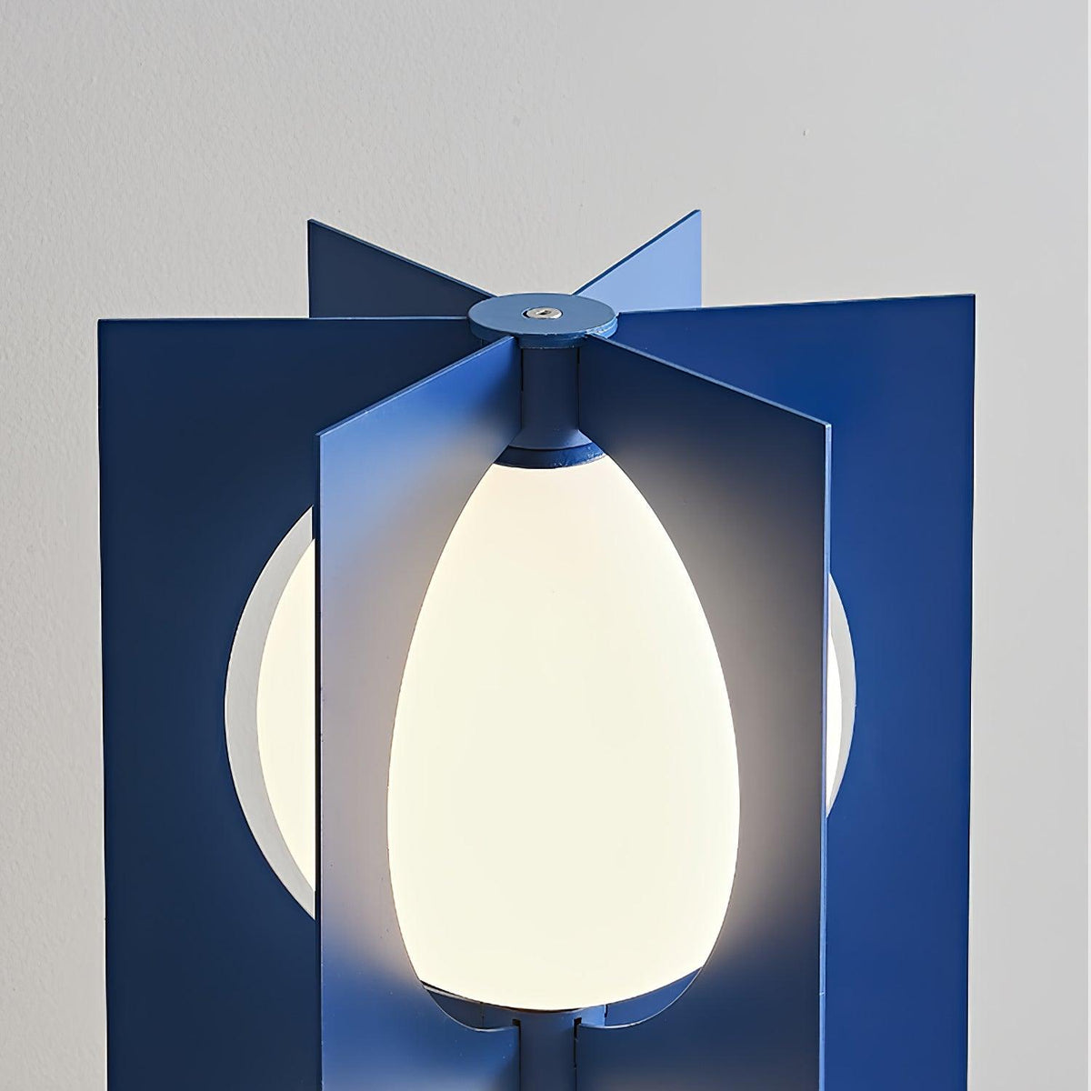 Close-up of the Clérachic floor lamp's egg-shaped glass shade glowing between two navy metal fins at the join.