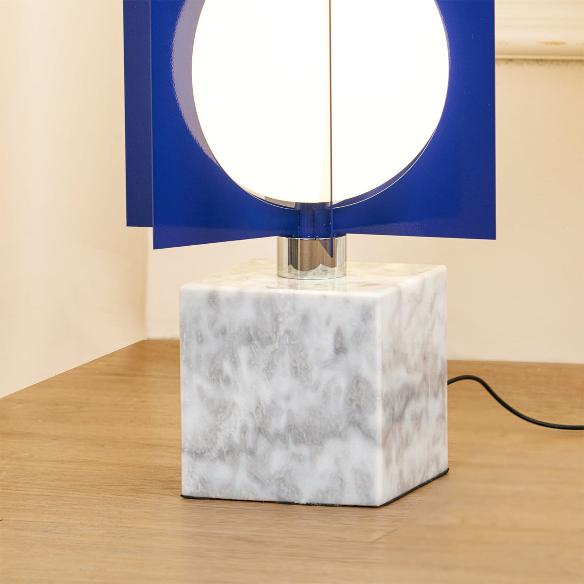 Close-up of the Clérachic lamp's white marble cube base and chrome column connector on a wood floor.