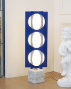 Three-globe Clérachic floor lamp glowing beside a cherub statue, set against a panelled wall and timber floor.