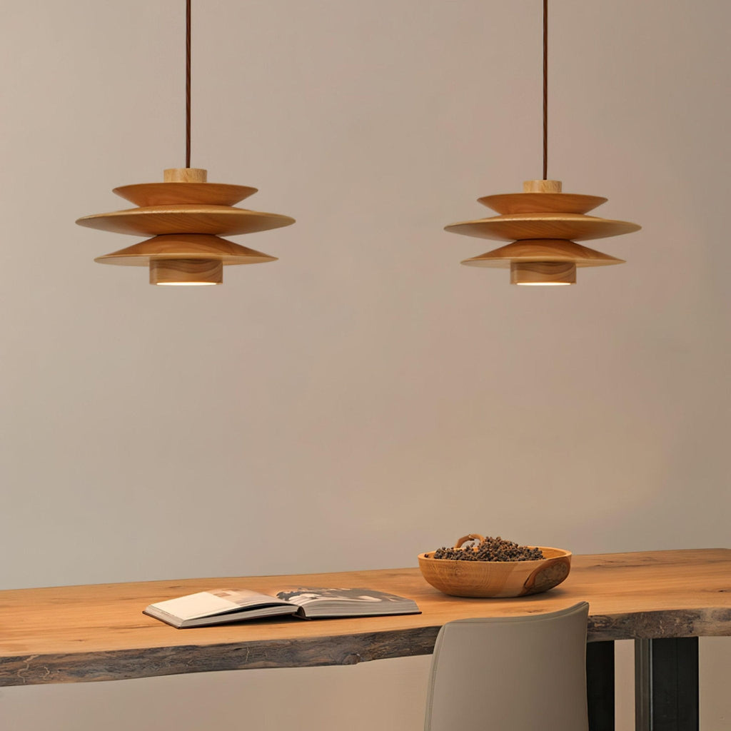 Two of this Clérachic pendant lamp in nature wood hang side by side above a pale desk with a bowl of pods.