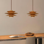 Two of this Clérachic pendant lamp in nature wood hang side by side above a pale desk with a bowl of pods.