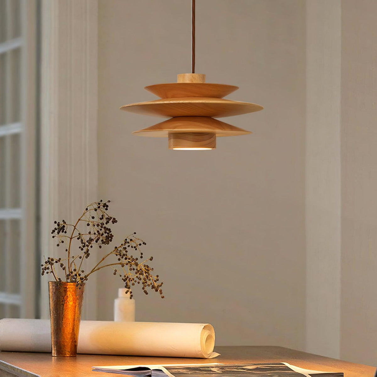 This Clérachic pendant lamp in nature wood hangs above a table with a copper vase of dried flowers and rolled papers.
