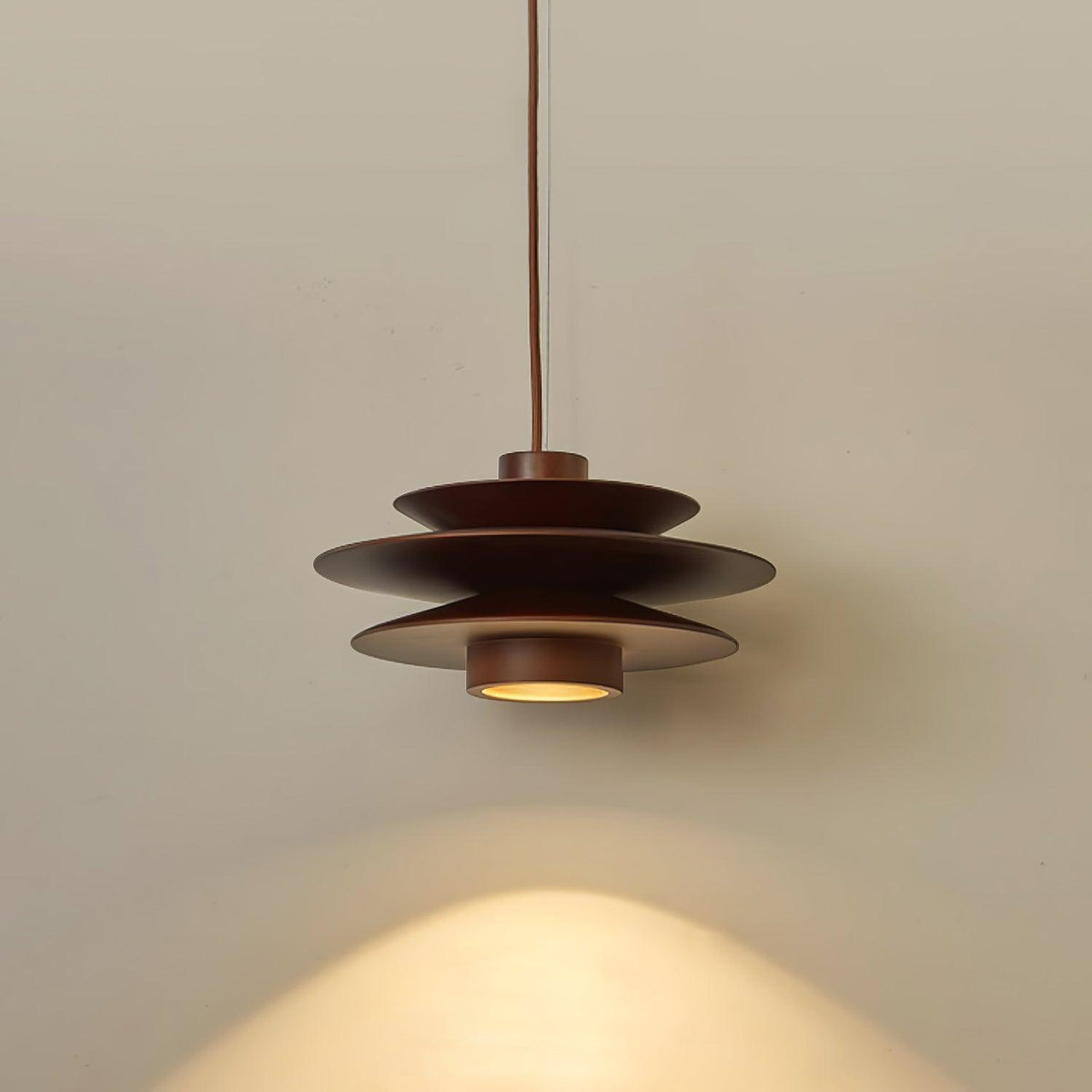Soft light catches the tiered shade of this Clérachic pendant in walnut wood against a plain grey backdrop.