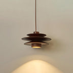 This Clérachic pendant in walnut wood hangs against a plain grey backdrop, its cord rising straight from the shade.