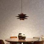 This Clérachic pendant in walnut wood glows above a round wood table set with two dark ceramic vases.