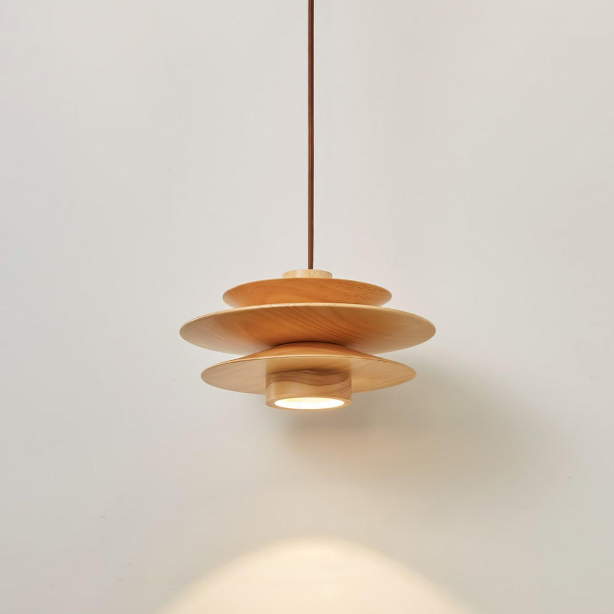 Against a plain grey backdrop, this Clérachic pendant in nature wood spreads warm light beneath its tiered discs.