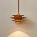An angled view of this Clérachic pendant in nature wood shows the top disc and cord against a grey backdrop.