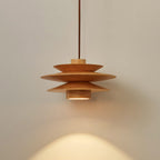 An angled view of this Clérachic pendant in nature wood shows the top disc and cord against a grey backdrop.