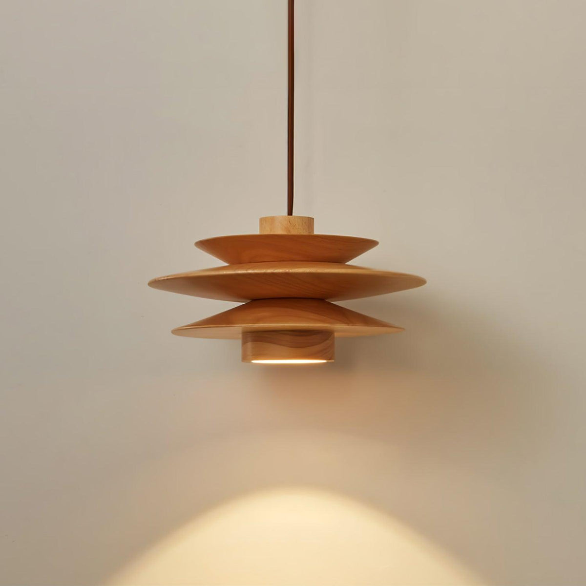 An angled view of this Clérachic pendant in nature wood shows the top disc and cord against a grey backdrop.