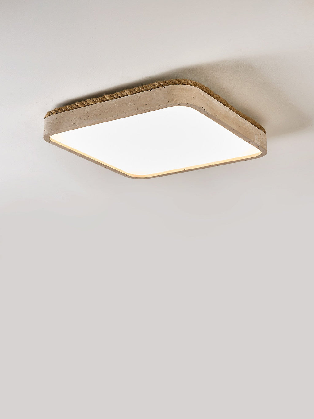 Side profile of this Clérachic flush mount light, its low travertine body and rope edge caught in soft grey light.