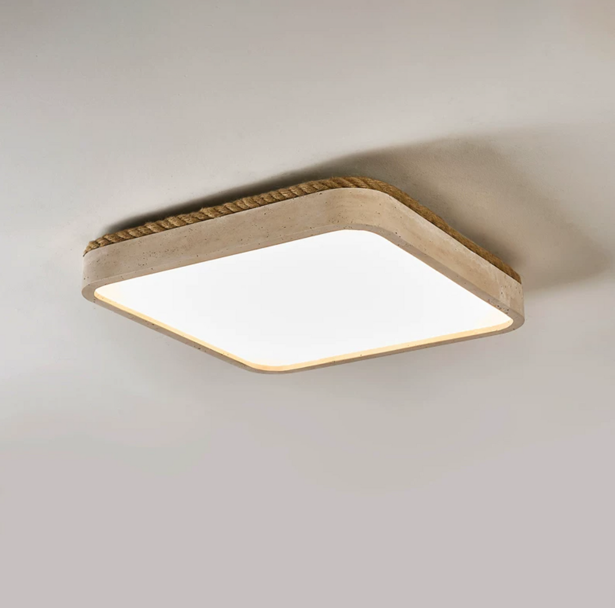 Angled view of this square Clérachic ceiling light in yellow travertine, showing its wound jute rope trim against a grey backdrop.