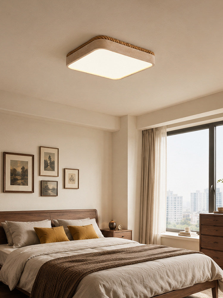 Warm light from this square Clérachic ceiling fixture fills a bedroom with mustard cushions and a city skyline through the window.