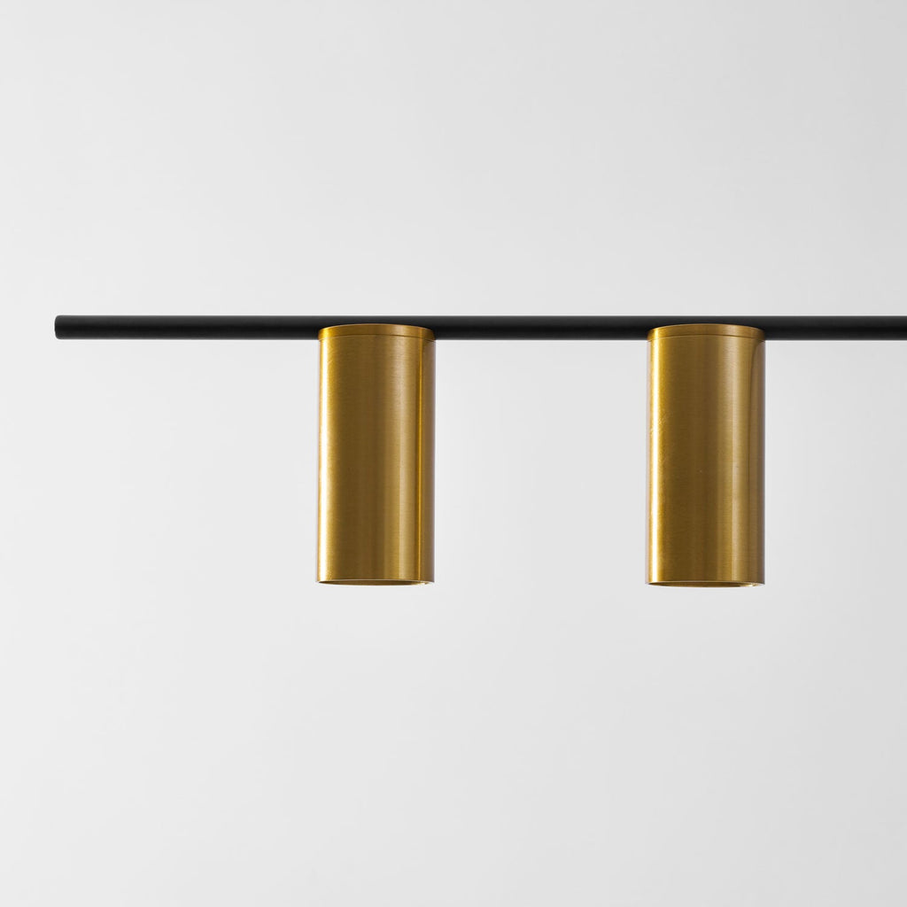 Close view of two brushed gold cylinder heads on the black bar of this Clérachic chandelier.