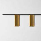 Close view of two brushed gold cylinder heads on the black bar of this Clérachic chandelier.