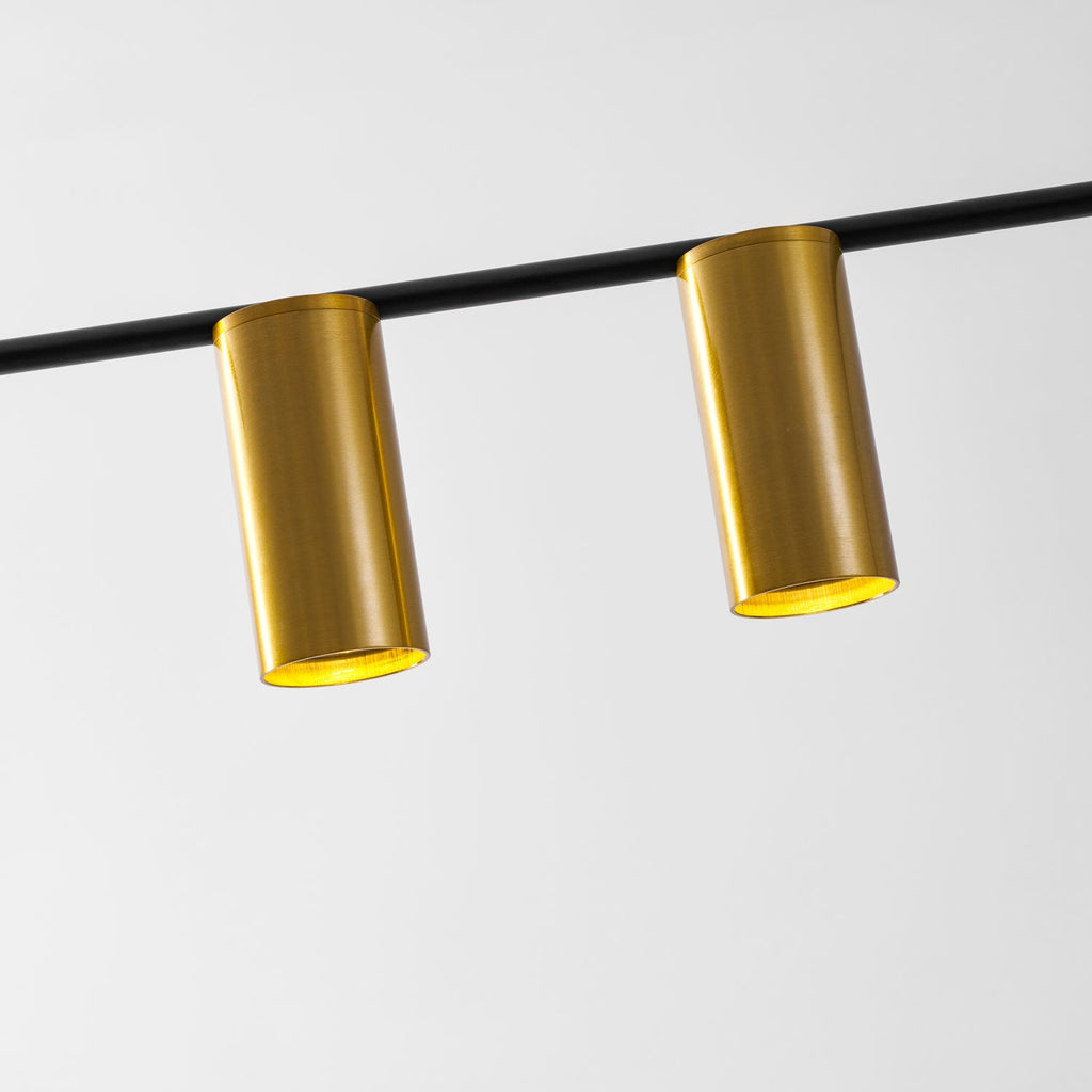 Close view of two brushed gold cylinder heads catching the light along this Clérachic chandelier's black bar.