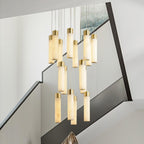 Aurelia chandelier over a modern staircase, alabaster tubes glowing against a dark glass balustrade.
