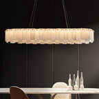 The long oval Aero chandelier lit above a marble dining table, glowing warm against a dark panelled wall