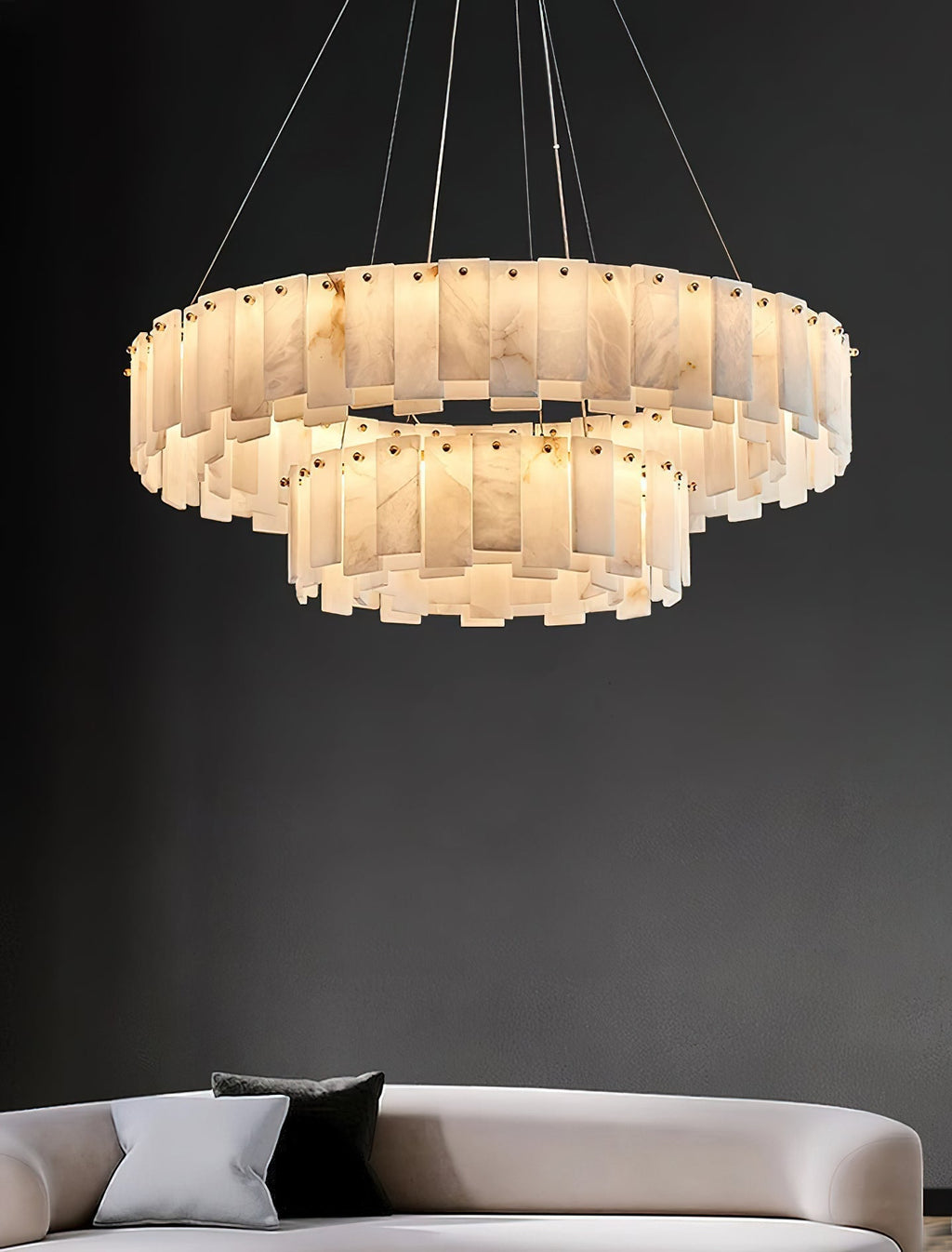 Aero round chandelier against a charcoal wall above a cream sofa, unlit so the stone reads pale grey