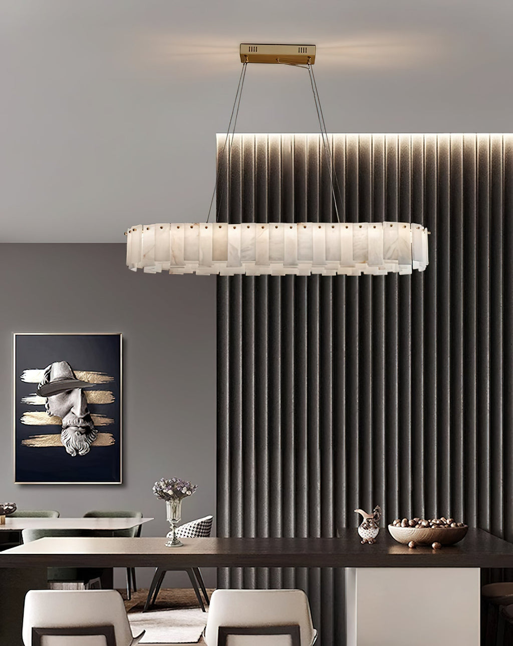 Long oval Aero chandelier lit over a dark dining table beside a fluted wall panel and framed artwork