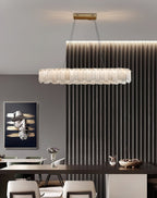 Long oval Aero chandelier lit over a dark dining table beside a fluted wall panel and framed artwork