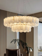 Aero round chandelier lit beside a city-view window, its two alabaster tiers seen from below