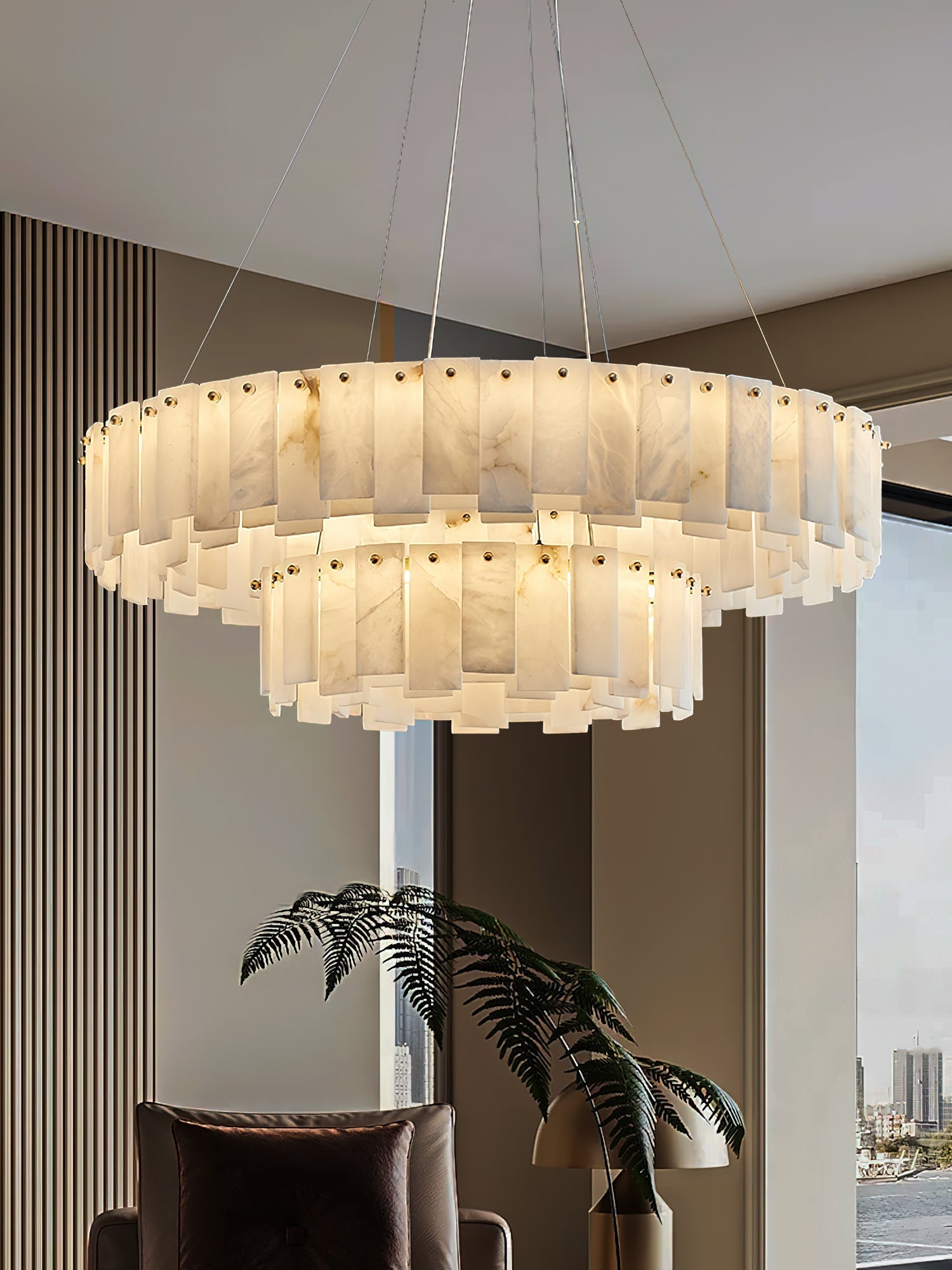 Aero round chandelier lit beside a city-view window, its two alabaster tiers seen from below