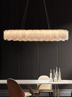 Aero chandelier's long oval version lit low over a marble dining table ringed with upholstered chairs