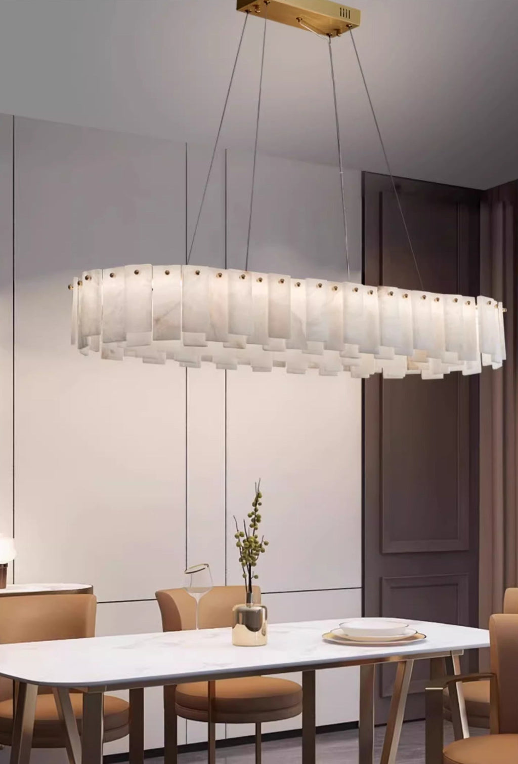 Long oval Aero chandelier lit above a white dining table, brass mounting bar visible on the ceiling